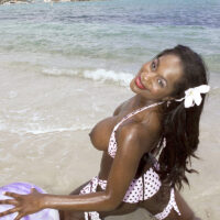 Ebony MILF Nikki Jaye lets out her enlargened tits from her bikini top while on a beach